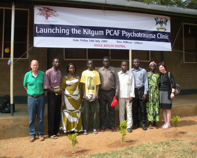 Picture in front of the new PCAF Clinic in Kitgum, Uganda where attendees of the workshop had the opportunity to experience daily life at a clinic.  Left to right:  Steve Alderman, co-founder of PCAF, member of PCAF Staff Kitgum;  Mary Grace Lanyero, PCO (psychiatric clinical officer), director of Kitgum Staff; James (child soldier); Dr. Henry Oboke, senior psychologist; member of PCAF Staff Kitgum;  member of PCAF Staff Kitgum;  Esther, patient at Kitgum Clinic and Liz Adlerman, co-founder of PCAF.  Note:  Background on Kitgum Clinic patients: James was kidnapped by the Lords Resistance Army and held in the bush for a number of years until he was able to escape.  