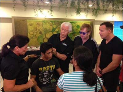 Sir Elton John, David Furnish and Starkey Hearing Foundation founders Bill and Tani Austin help a young man hear during the Foundations mission in Manila, Philippines on December 8