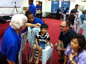  NFL Player Larry Fitzgerald observes Bill Austin, Founder, Starkey Hearing Foundation, as he fits a young patient with a hearing device during the Foundations recent hearing mission in Malaysia