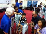  NFL Player Larry Fitzgerald observes Bill Austin, Founder, Starkey Hearing Foundation, as he fits a young patient with a hearing device during the Foundations recent hearing mission in Malaysia