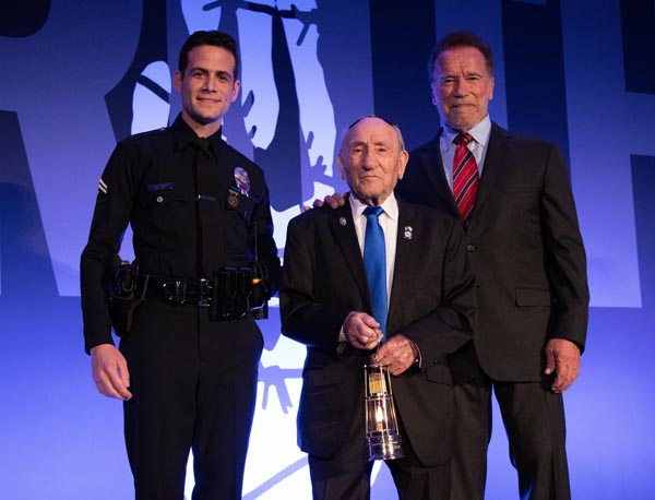 Former California Governor, actor and businessman Arnold Schwarzenegger and 101-year-old Holocaust survivor Joe Alexander handing museums Eternal Flame in a special created miners lamp to LAPDs Officer Gabe Cohen at the museum's 15th annual gala held at the Beverly Hills Hotel for police escort of the flame through the streets of LA to its permanent home at the museum.